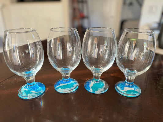 Tulip shaped beer glasses, decoration with resin ocean waves on the base of the glasses. The waves are blue, turquoise, and white foam.