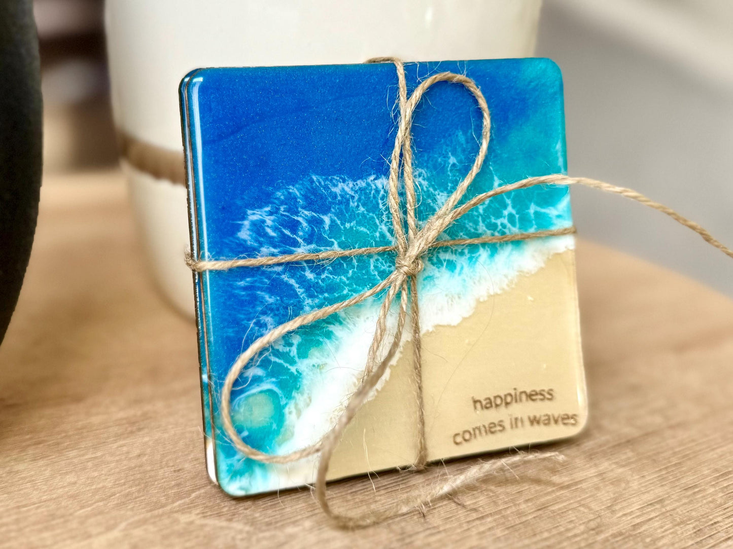 Wood coaster set with resin ocean waves and"happiness comes in waves" engraved in the sand area of the beach scene.