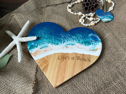 Coastal wall art, wooden heart with ocean waves and "Life's a beach" engraved in the sand area of the beach scene.