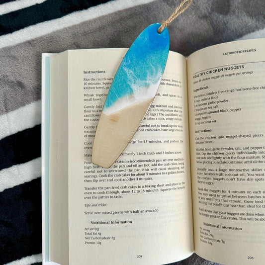 Surfboard bookmark with resin ocean waves in blue and turquoise with white foam against a sandy beach. Personalized on the back.