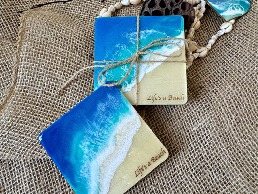 Square wood coaster set with resin ocean waves and &quot;Life&#39;s a Beach&quot; engraved in the sand area of the coasters.