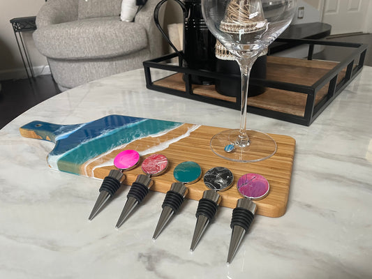 Five wine bottle stoppers, hand painted in bright pink, red and white swirl, turquoise, black and white swirl, and purple and pink swirl. The stoppers are stainless steel with painted toppers.